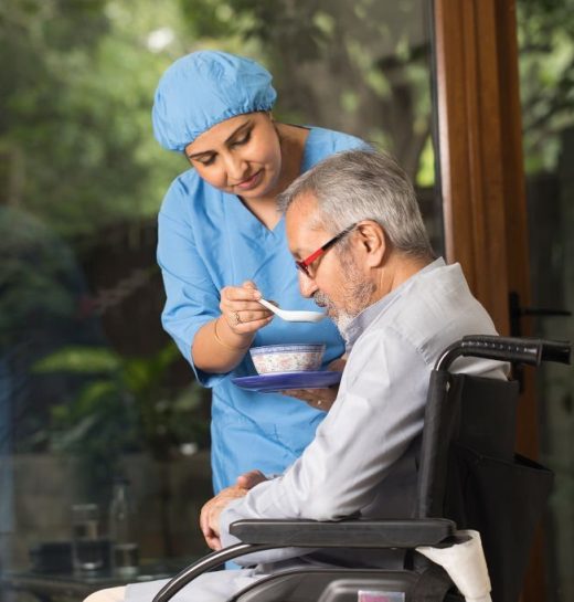 Female caregiver feeding food to disabled senior man on wheelchair
